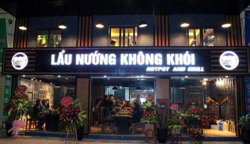 Mặt tiền quán lẩu nướng không khói về đêm với bảng chữ trắng và kính trong suốt