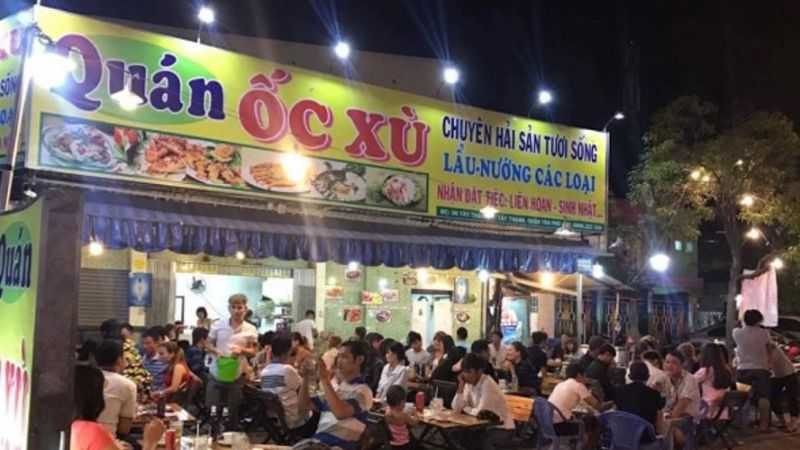 Quán ốc về đêm đông khách với bảng in hình món ăn và đèn chiếu phía trên