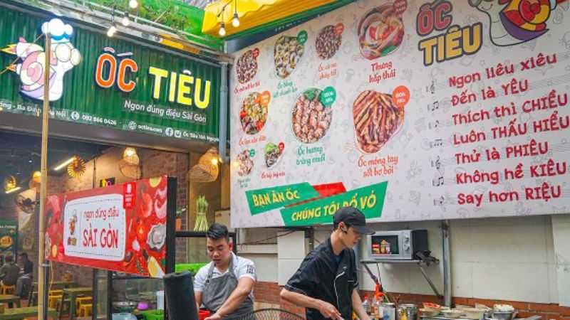 Quán Ốc Tiêu với bảng xanh lá và mảng tường in hình các món ốc kèm câu chữ vui