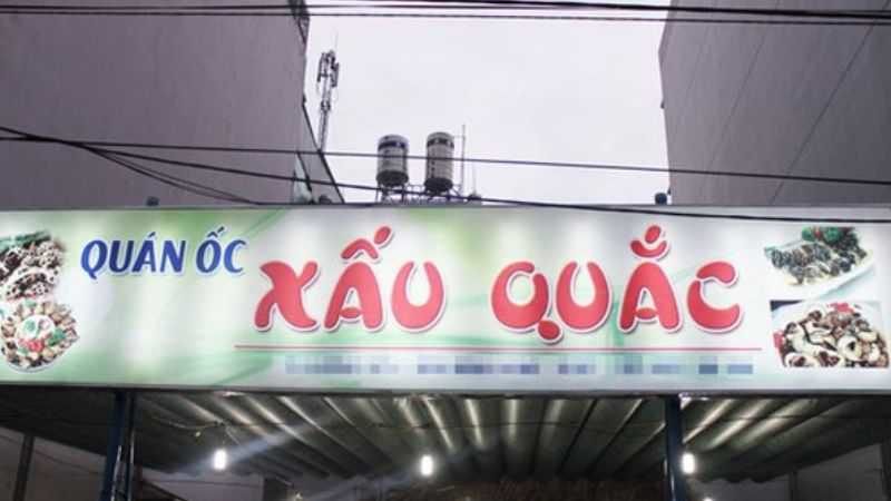 Bảng hiệu quán ốc Xấu Quắc nền trắng xanh, chữ đỏ cách điệu và hình ốc hai bên