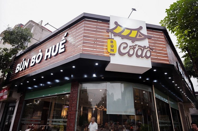 Quán bún bò Huế ở góc phố với mặt dựng lam gỗ và logo nón lá
