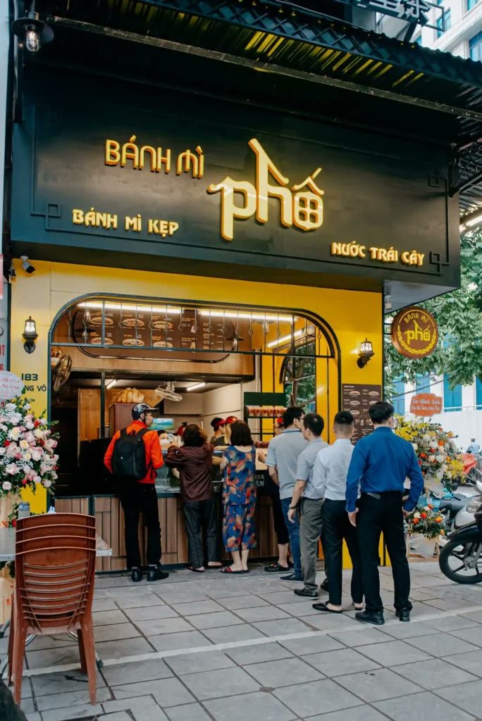Tiệm Bánh mì Phố với mặt tiền xanh đậm, chữ vàng và khách xếp hàng