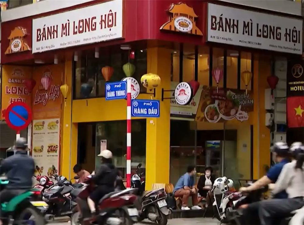 Tiệm Bánh mì Long Hội ở góc phố với mặt tiền vàng và bảng hiệu chạy hai mặt