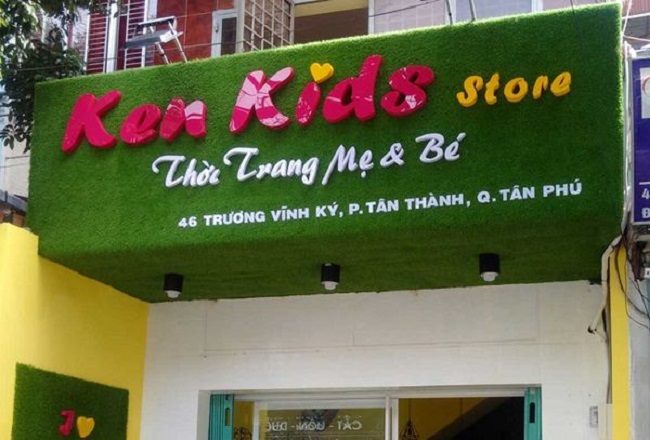 Bảng hiệu Ken Kids Store chữ nổi hồng trên nền cỏ nhân tạo xanh