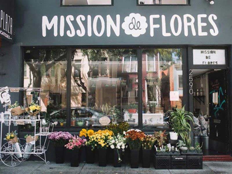 Mặt tiền shop hoa nền xám đậm chữ trắng lớn, hoa bày trên vỉa hè