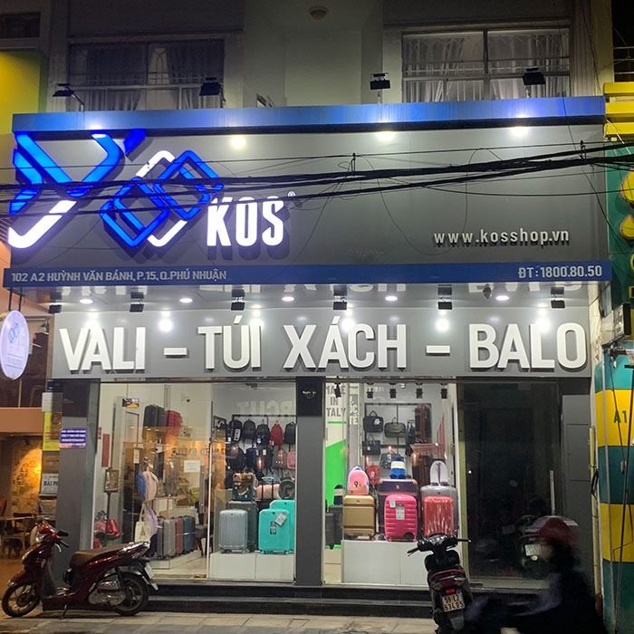 Cửa hàng KOS về đêm với logo LED xanh và chữ nổi Vali Túi xách Balo trên nền alu xám