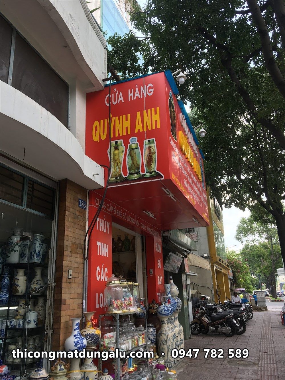 Cửa hàng Quỳnh Anh ở góc phố, bảng hiệu đỏ ngang và bảng đứng trên trụ