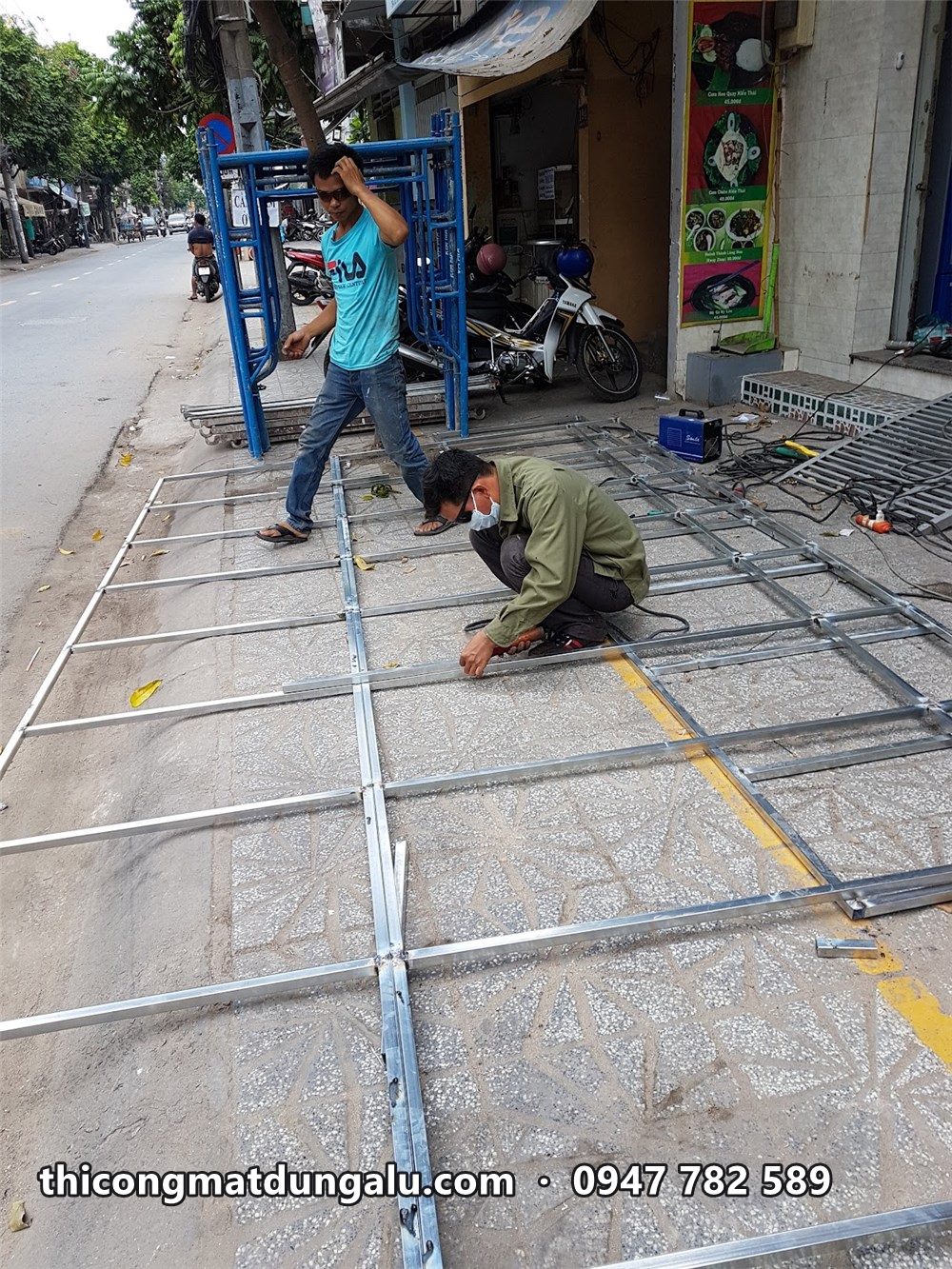 Thợ lắp khung sắt bảng hiệu nằm trên vỉa hè trước cửa hàng