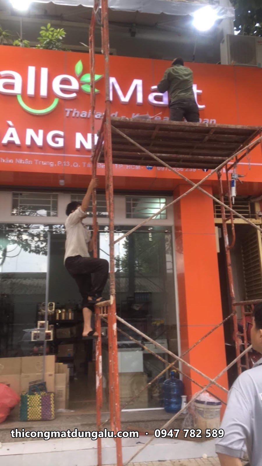 Thợ trên giàn giáo gắn chữ Alle Mart lên nền cam