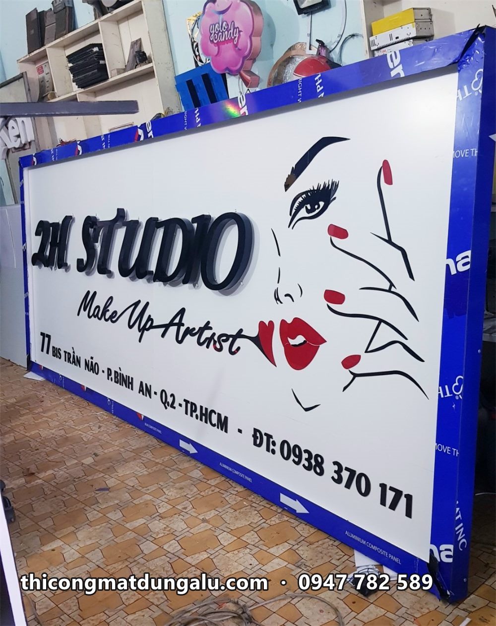 Bảng hiệu 2H Studio Make Up Artist nền trắng in gương mặt phụ nữ, chữ nổi đen, đặt trong xưởng