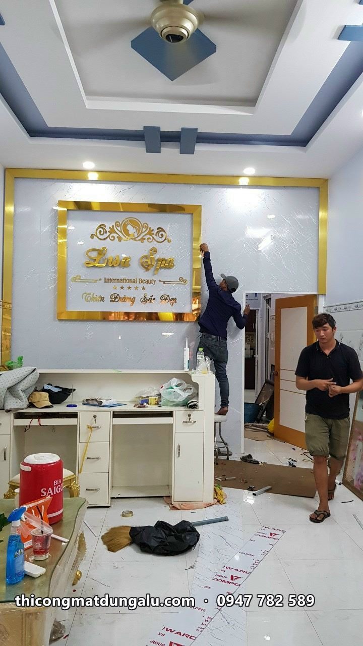 Thợ gắn logo chữ vàng lên tường trắng trong tiệm, viền khung vàng