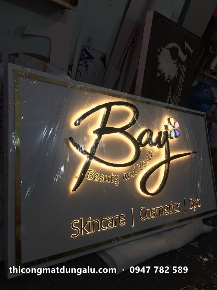 Bảng hiệu Bay Beauty chữ viết tay hắt sáng vàng trên nền xám, dòng Skincare Cosmetics Spa