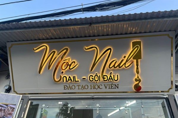 Bảng hiệu tiệm nail chữ inox vàng hắt sáng trên nền trắng viền vàng