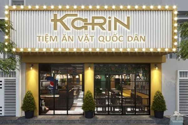 Tiệm ăn vặt mặt tiền trắng, chữ nổi vàng đồng và viền bóng đèn tròn quanh bảng hiệu