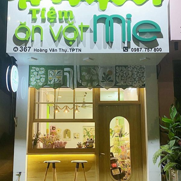 Tiệm ăn vặt nhà ống hẹp với chữ viết tay màu xanh lá và cửa sổ vòm