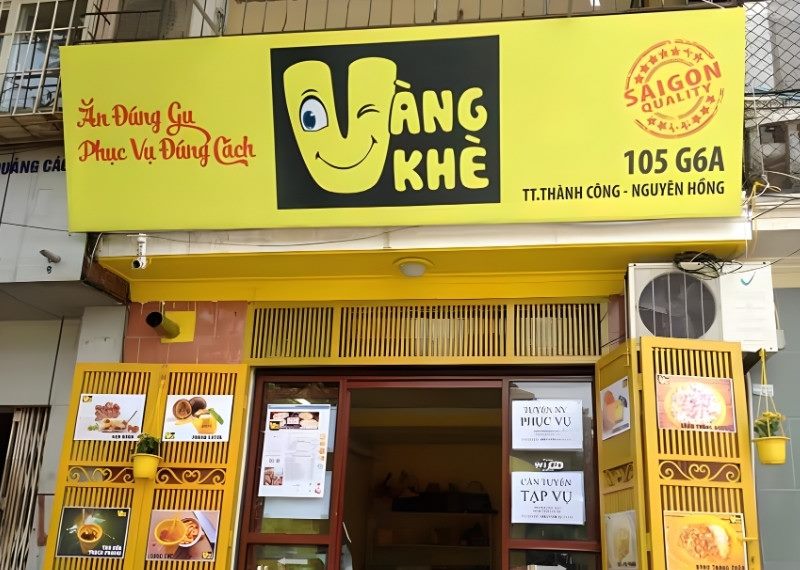 Tiệm ăn vặt nền vàng với logo mặt cười chữ V, khung cửa sơn vàng đồng bộ