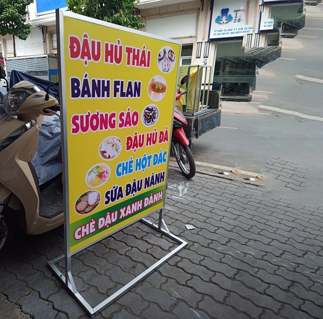 Standee khung sắt in menu đậu hũ, bánh flan, sương sáo đặt trên vỉa hè