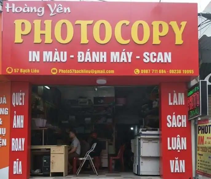 Bảng hiệu tiệm photocopy nền đỏ, chữ vàng lớn và biển dọc hai bên cửa