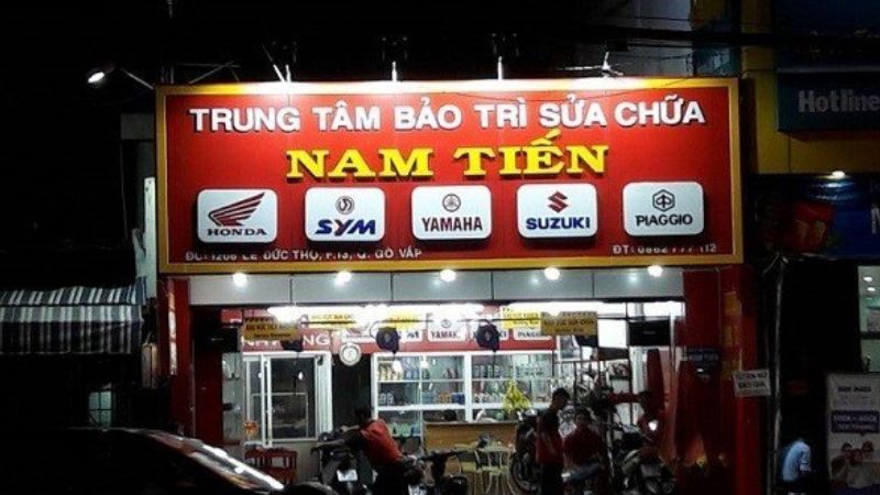 Tiệm sửa xe về đêm, bảng hiệu đỏ có hàng logo hãng xe sáng đèn