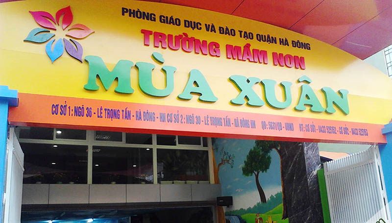 Bảng hiệu trường mầm non nền vàng cam, chữ nổi xanh lớn và hoa trang trí