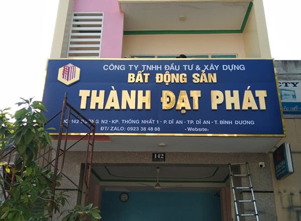 Bảng hiệu công ty bất động sản nền xanh dương chữ vàng gắn trên tầng trệt nhà phố