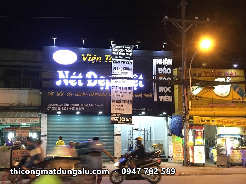 Viện tóc Nét Đẹp Việt sáng đèn ban đêm, xe máy chạy qua