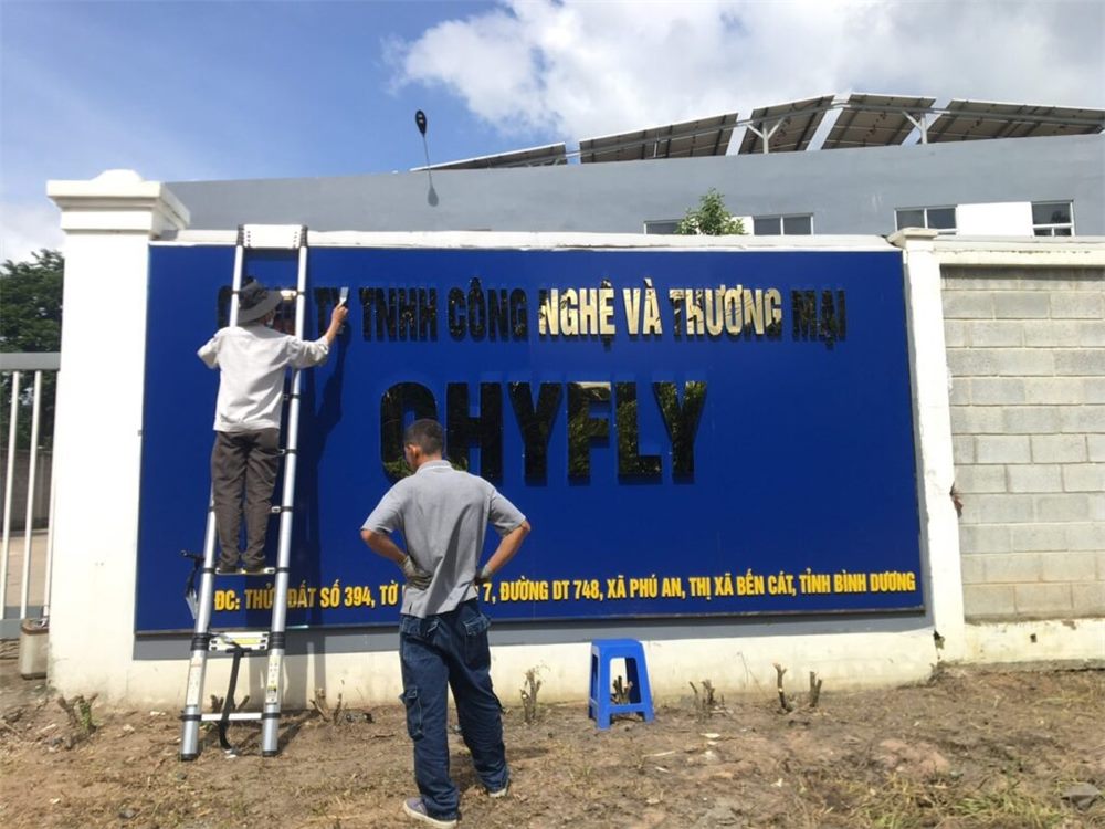 Hai thợ đang gắn chữ lên bảng tên công ty nền xanh ở cổng