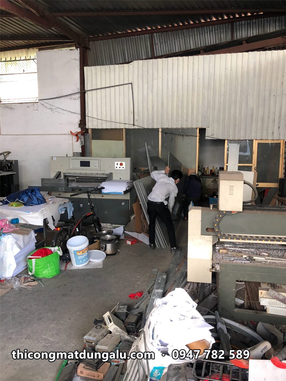 Bên trong xưởng mái tôn với máy cắt và vật tư, thợ đang làm việc