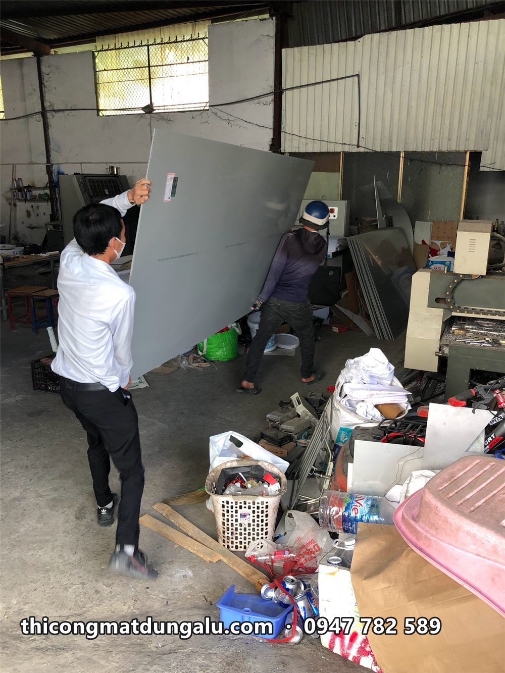 Hai người khiêng tấm alu khổ lớn trong xưởng