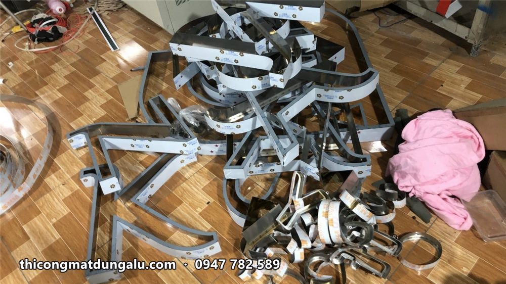 Các thân chữ inox chưa có mặt nằm chồng trên sàn gỗ