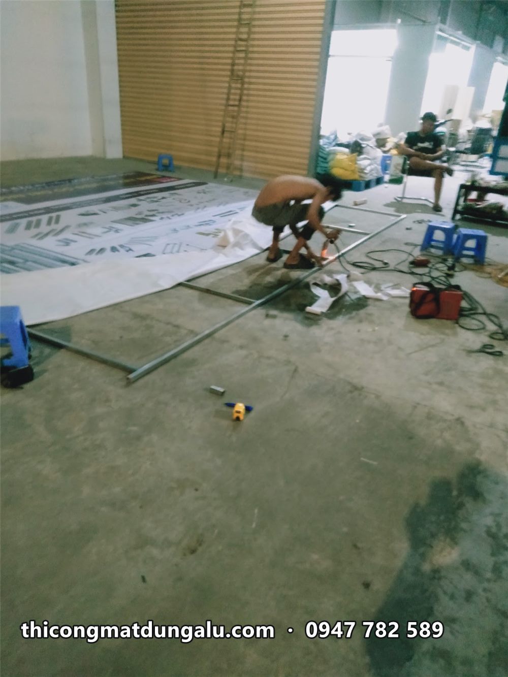 Thợ hàn khung sắt trên tấm bạt in trải trên sàn xưởng