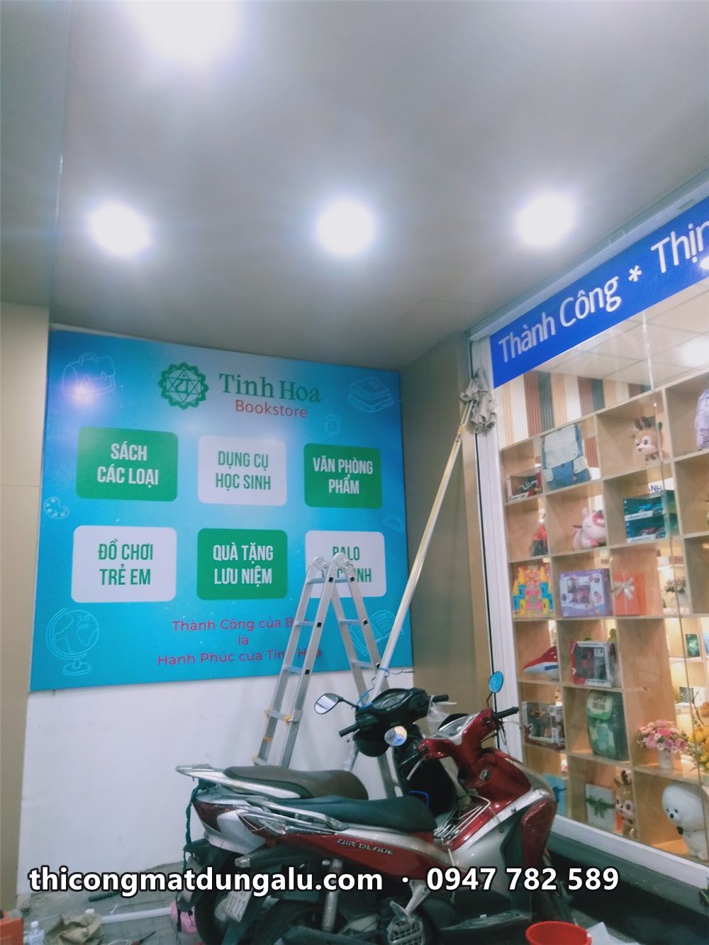 Tường danh mục nhà sách nhìn nghiêng, kệ hàng bên phải, xe máy phía trước