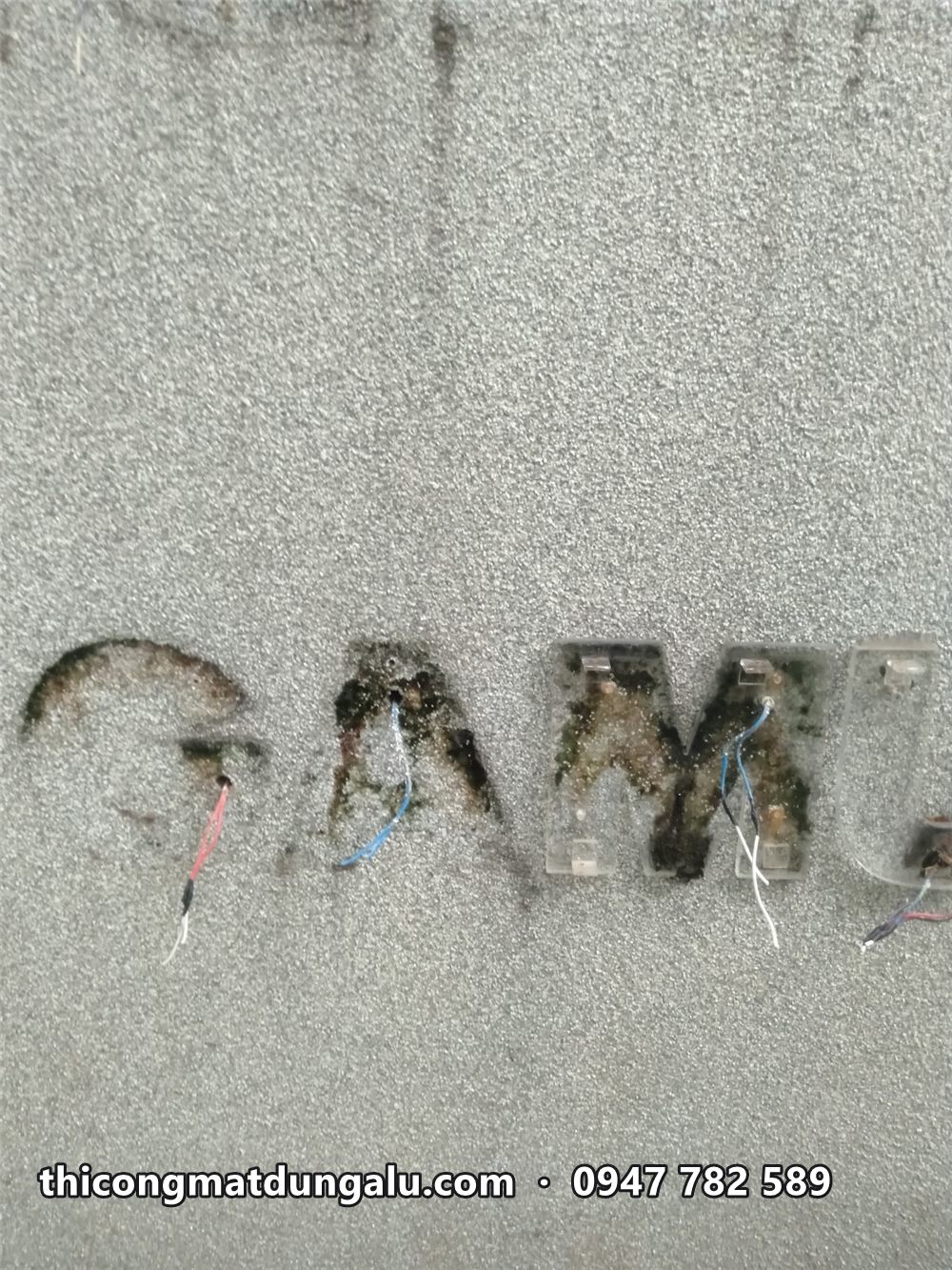 Tường sơn gai sau khi tháo chữ GAMUDA cũ, còn vết keo đen và đầu dây điện