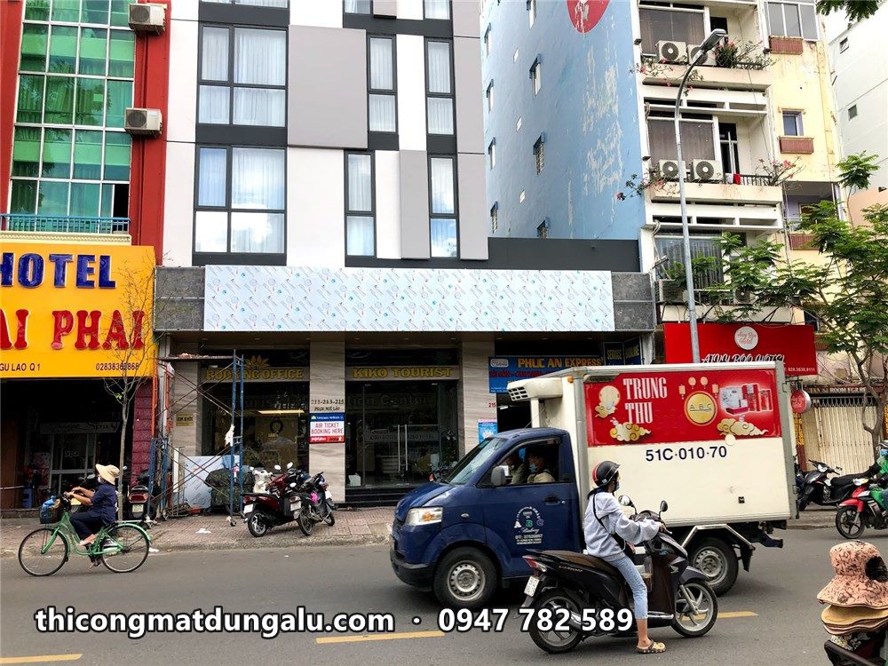 Mặt tiền khách sạn Megustas nhiều tầng giữa dãy phố, xe tải và xe máy phía trước
