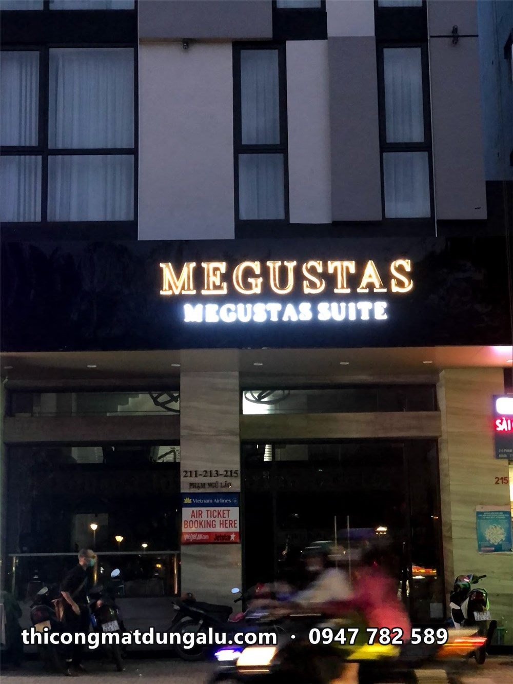 Chữ Megustas Megustas Suite sáng trên mái đón ban đêm, xe máy chạy qua