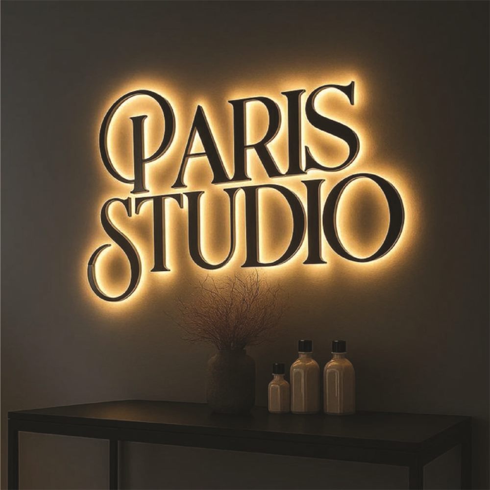 Logo studio chữ đen hắt sáng vàng ấm trên tường xám tối