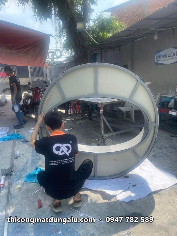 Thợ ngồi lắp mặt mica cho chữ O tròn cỡ lớn ngoài sân xưởng
