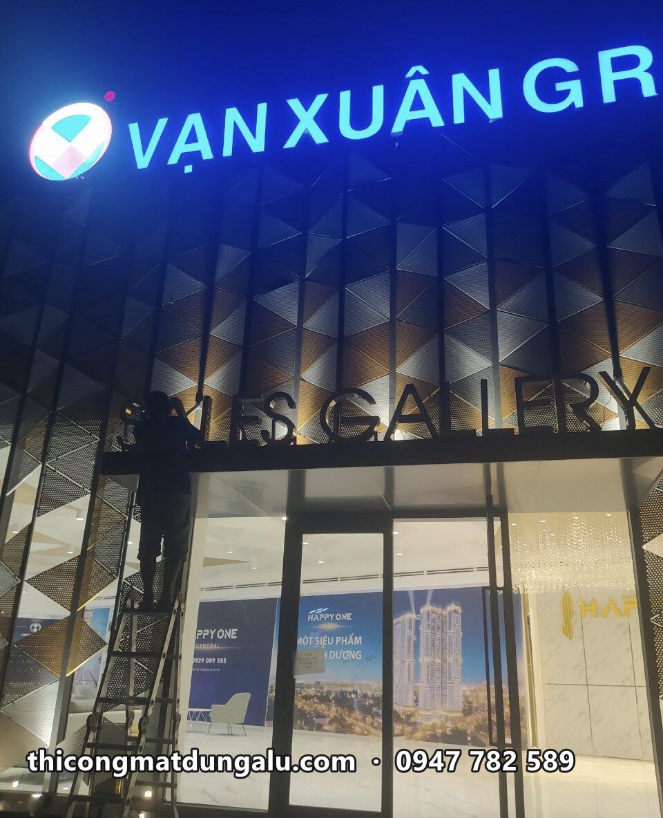 Chữ Vạn Xuân Group sáng đèn phía trên lối vào Sales Gallery, thợ đứng thang lắp đặt