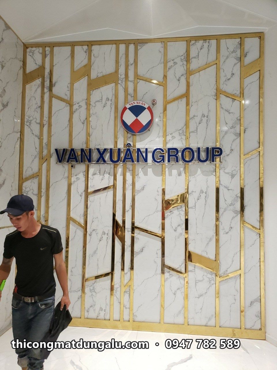 Thợ đứng cạnh vách đá có logo Vạn Xuân Group giữa các thanh inox vàng