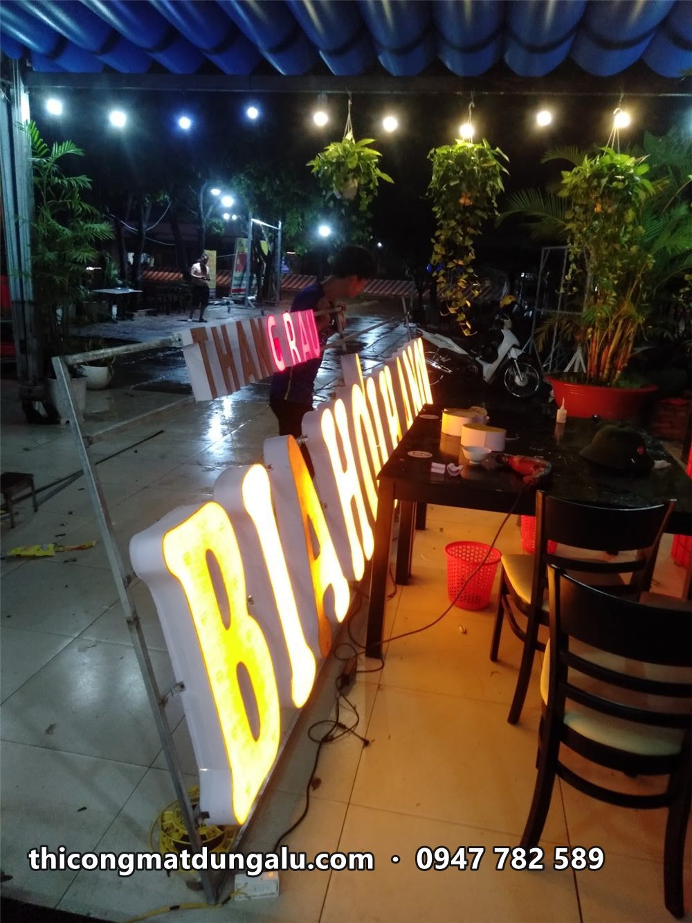 Chữ BIA HƠI sáng vàng khi thử đèn ban đêm trong quán, cạnh bàn ghế gỗ