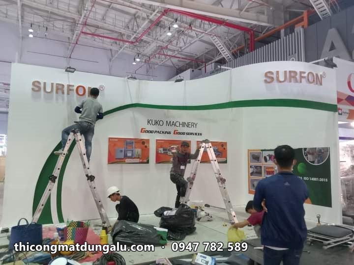 Thợ trên thang lắp gian hàng Surfon trắng với đường cong xanh lá, logo đỏ