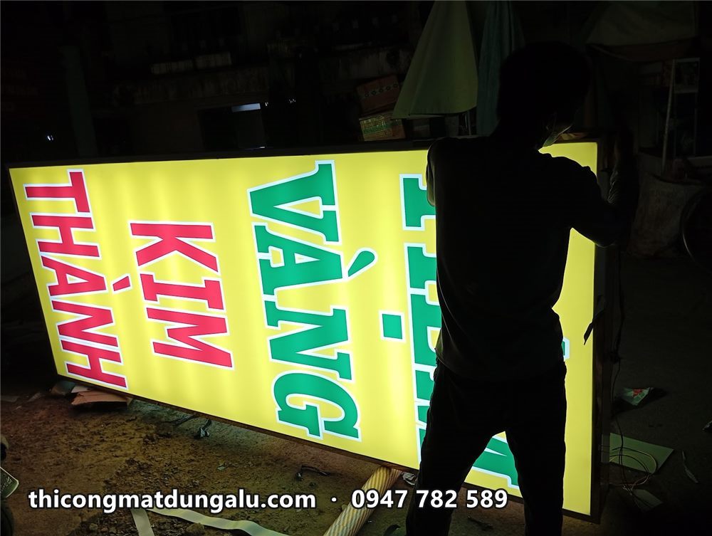 Thợ kiểm tra mép hộp đèn Tiệm Vàng Kim Thành đang sáng trong xưởng