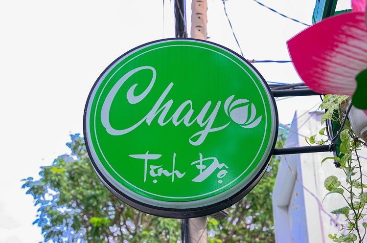 Hộp đèn tròn mặt xanh lá treo vuông góc trước quán chay