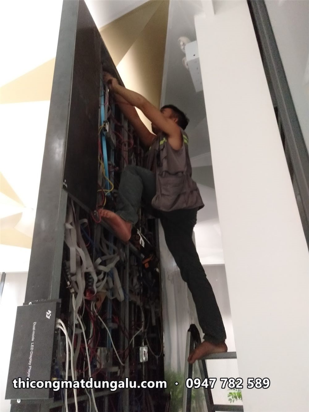 Thợ trèo lên khung sau màn hình LED để đấu nối dây nguồn