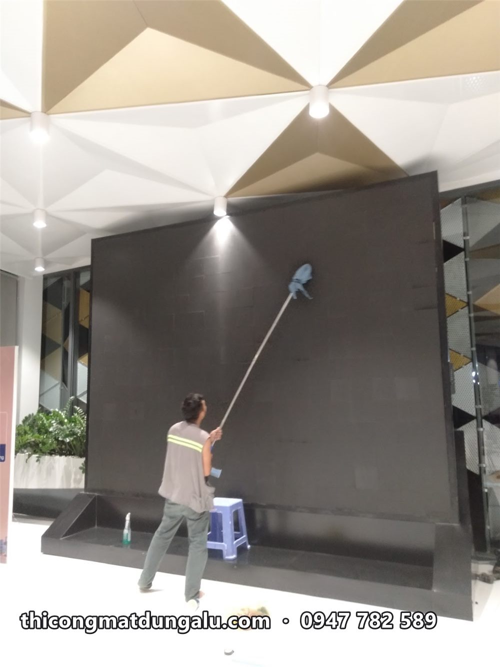 Thợ đứng trên ghế dùng cây lau cán dài vệ sinh mặt màn hình LED