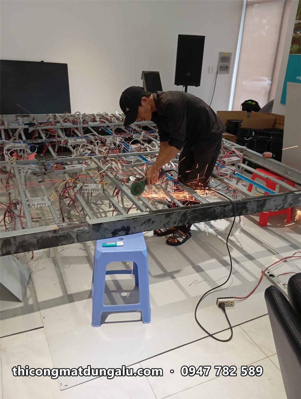 Thợ cắt khung thép màn hình LED ngay trong hội trường, bên cạnh ghế nhựa và dụng cụ