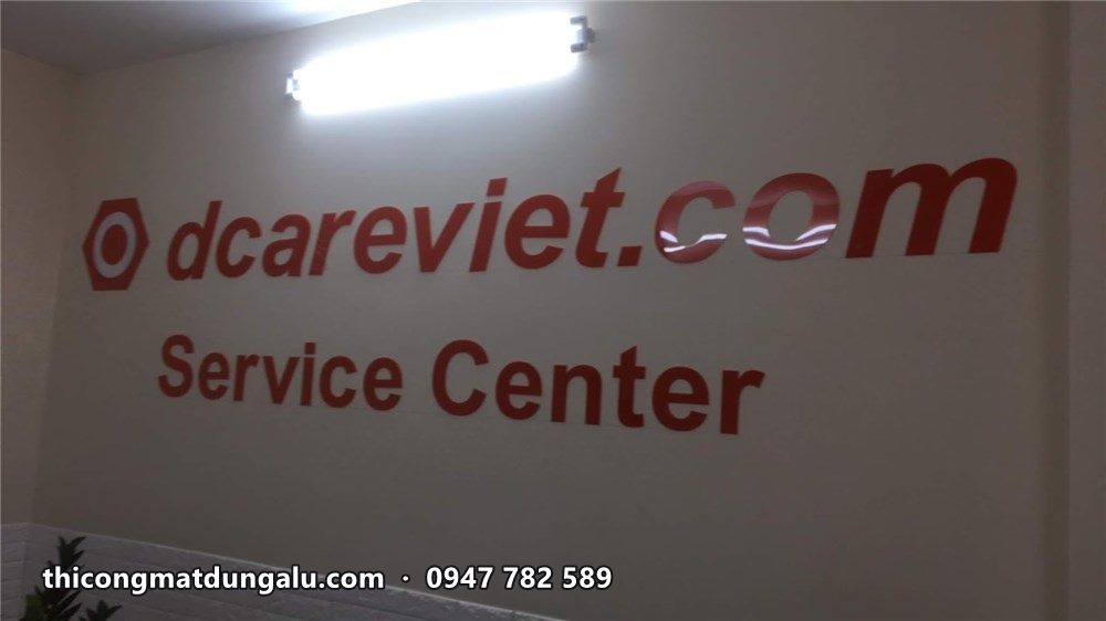 Chữ dcareviet.com Service Center màu cam đỏ đang gắn trên tường trắng