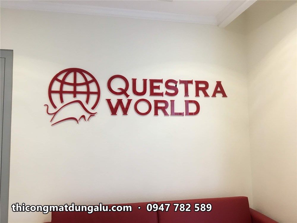 Logo Questra World đỏ đô gắn tường trắng phía trên ghế sofa đỏ