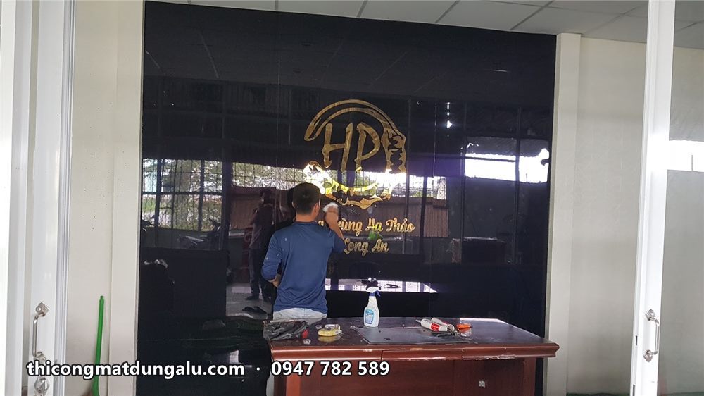 Thợ đứng sau bàn gỗ gắn logo inox vàng lên vách kính