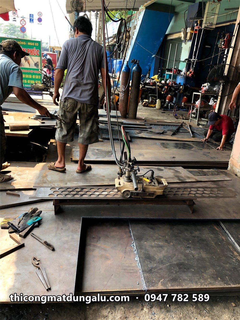 Thợ gia công tấm alu trên mặt đất cạnh công trình